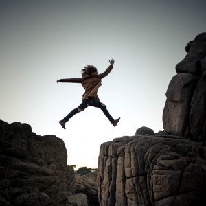 girl jumping across a cliff ridge